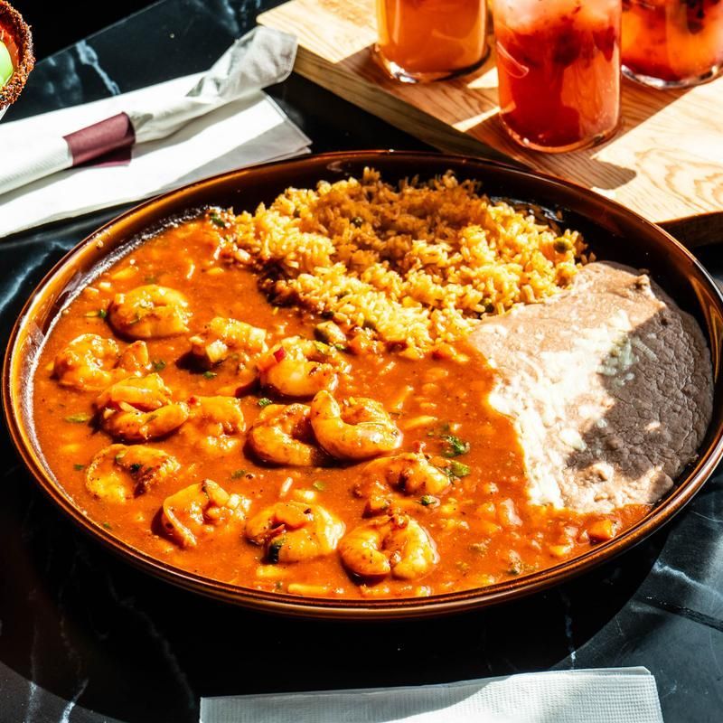 Tray of orange curry with rice and bread on a restaurant table, with drinks in the background