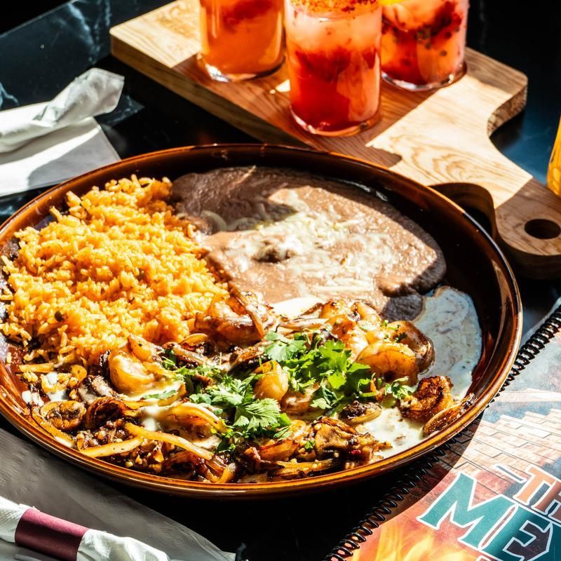 Mexican meal with rice, refried beans, enchiladas, and salad on a wooden table with pink drinks