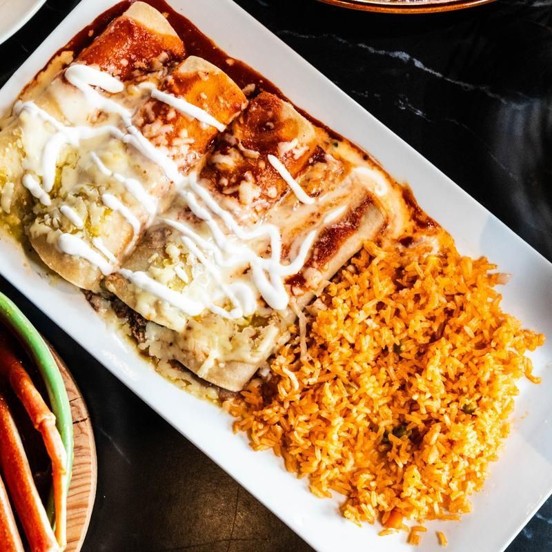 Enchiladas topped with white sauce beside a mound of seasoned rice on a white plate
