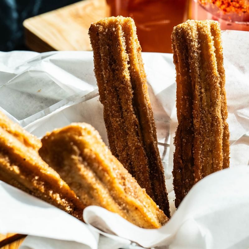 Golden churros in a white paper tray, dusted with sugar, on a bright table.