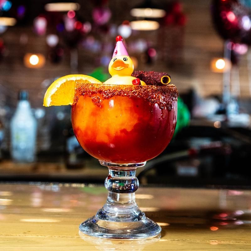 Red cocktail in a stemmed glass with orange slice, cinnamon stick, and a tiny Santa hat garnish