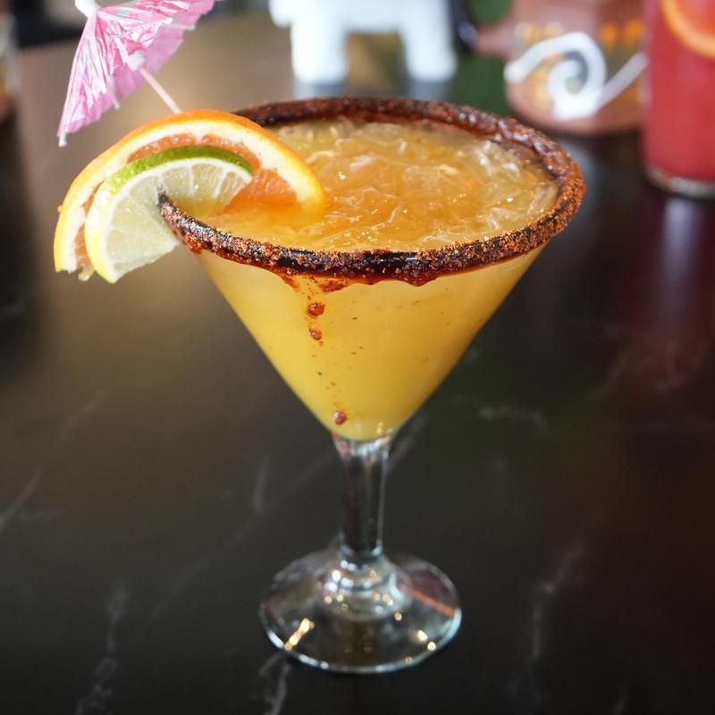 Margarita with a sugar-rimmed glass, orange slice garnish, and pink umbrella on a dark table