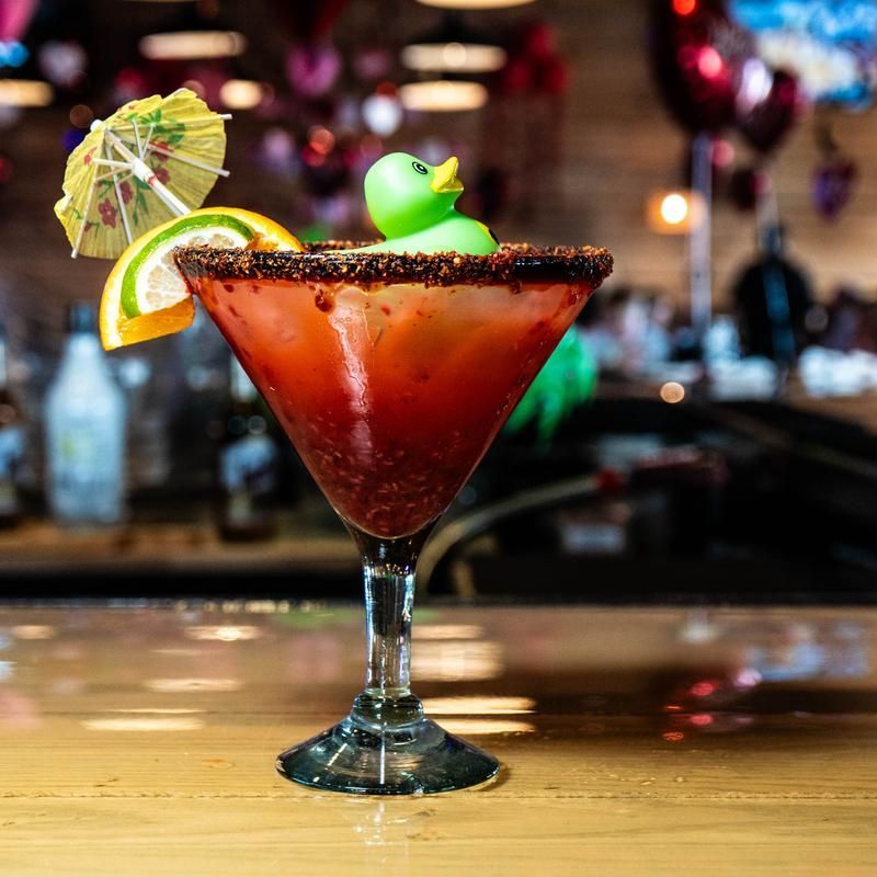 Red cocktail in a martini glass with a citrus garnish and umbrella on a bar counter
