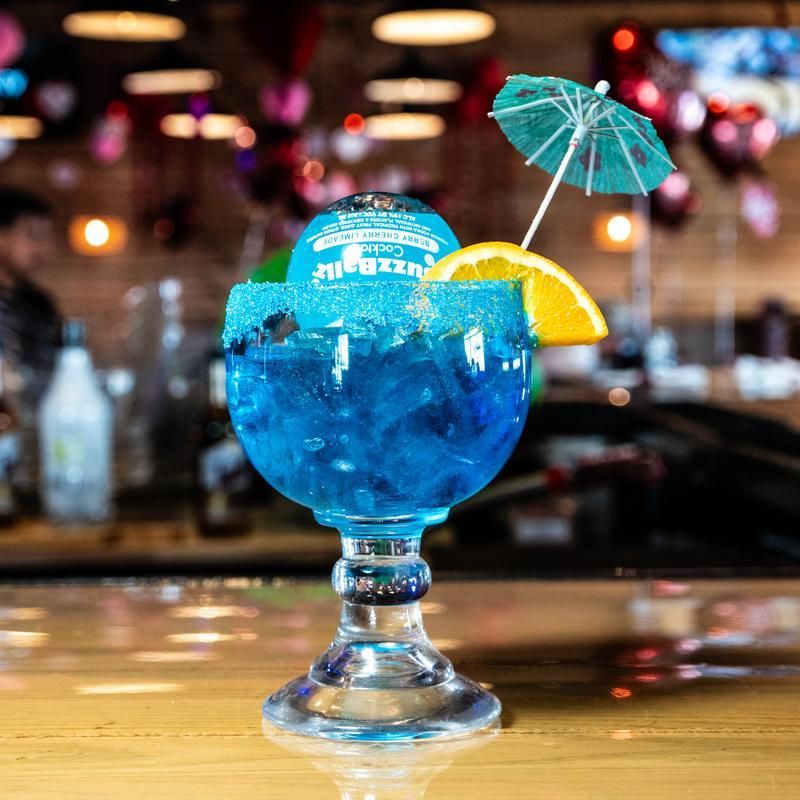 Blue tropical cocktail in a stemmed glass with a paper umbrella and orange slice on a bar counter