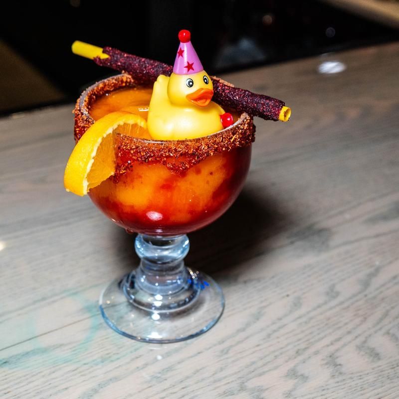 Festive dessert cocktail in a stemmed glass, garnished with orange peel, candy sticks, and a duck topper