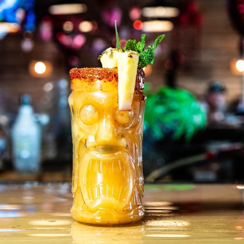 Tropical tiki cocktail with pineapple garnish and mint in a carved tiki glass on a bar counter