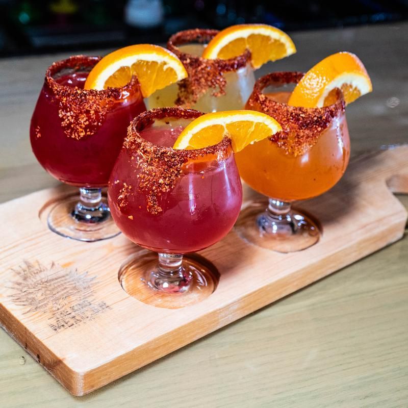 Four orange-garnished red cocktails on a wooden tray