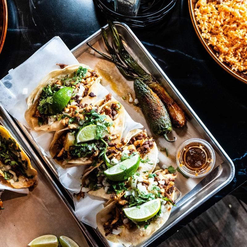 Tacos on a metal tray with lime wedges and salsa, viewed from above.
