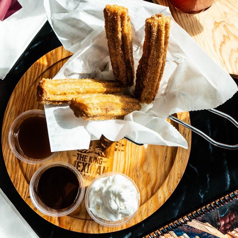 Churros on a wooden tray with three dipping sauces on a table