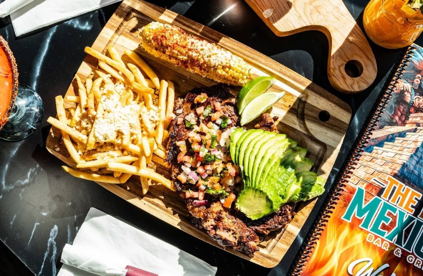 Mexican meal tray with fries, burrito, avocado slices, and salsa on a dark table