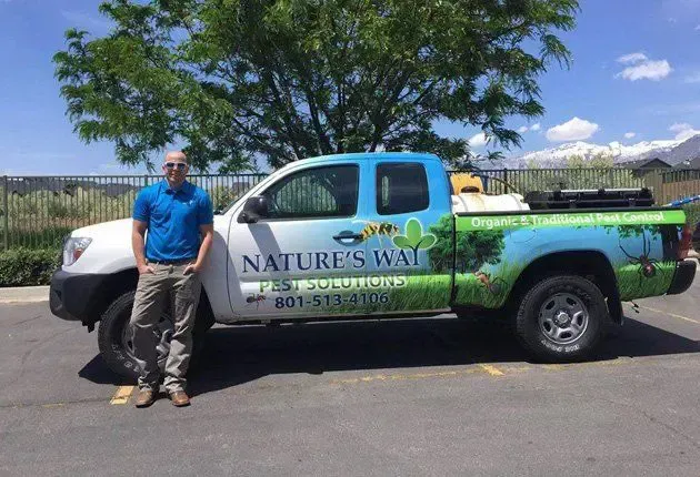 Man standing beside a Nature's Way service truck in a sunny parking lot.