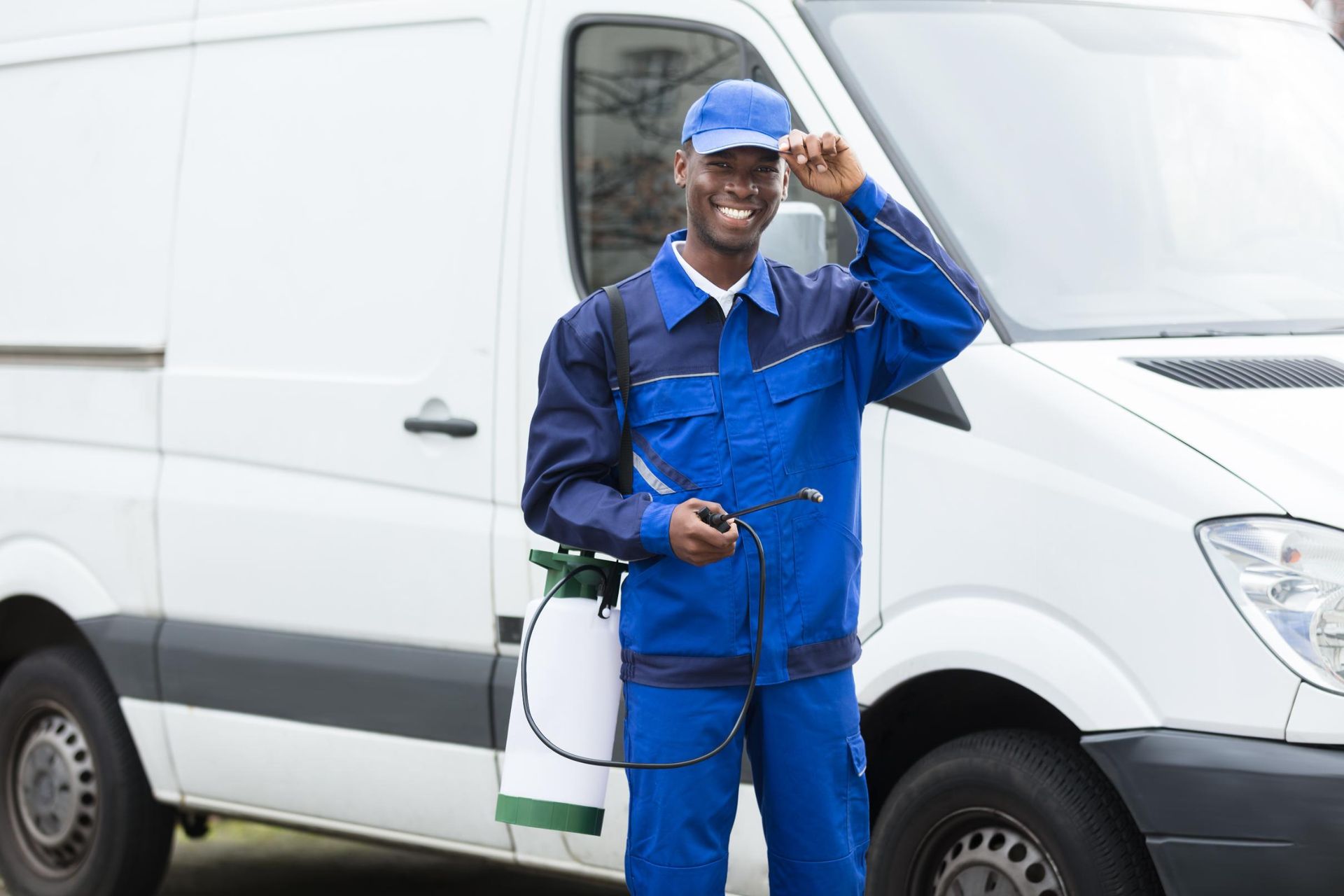 Worker in blue coveralls adjusting his hard hat beside a white service van.