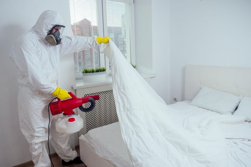 Person in hazmat suit disinfecting a white bedroom with a sprayer