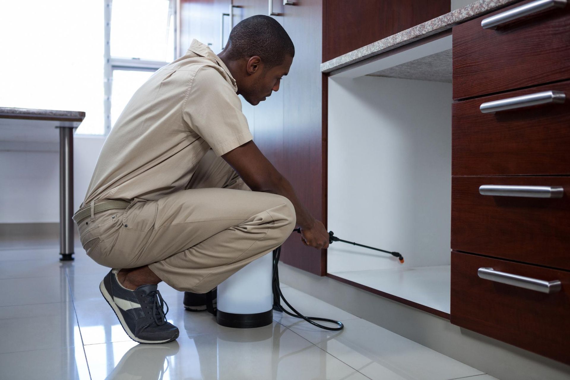 Person crouching beside a kitchen cabinet, using a tool near a water valve.