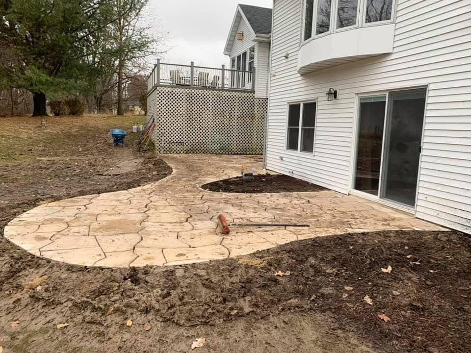 Curved stone patio beside a white house with sliding glass door and bare yard landscaping