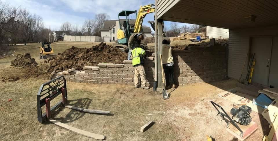 Construction workers and excavator building a stone retaining wall under a house deck