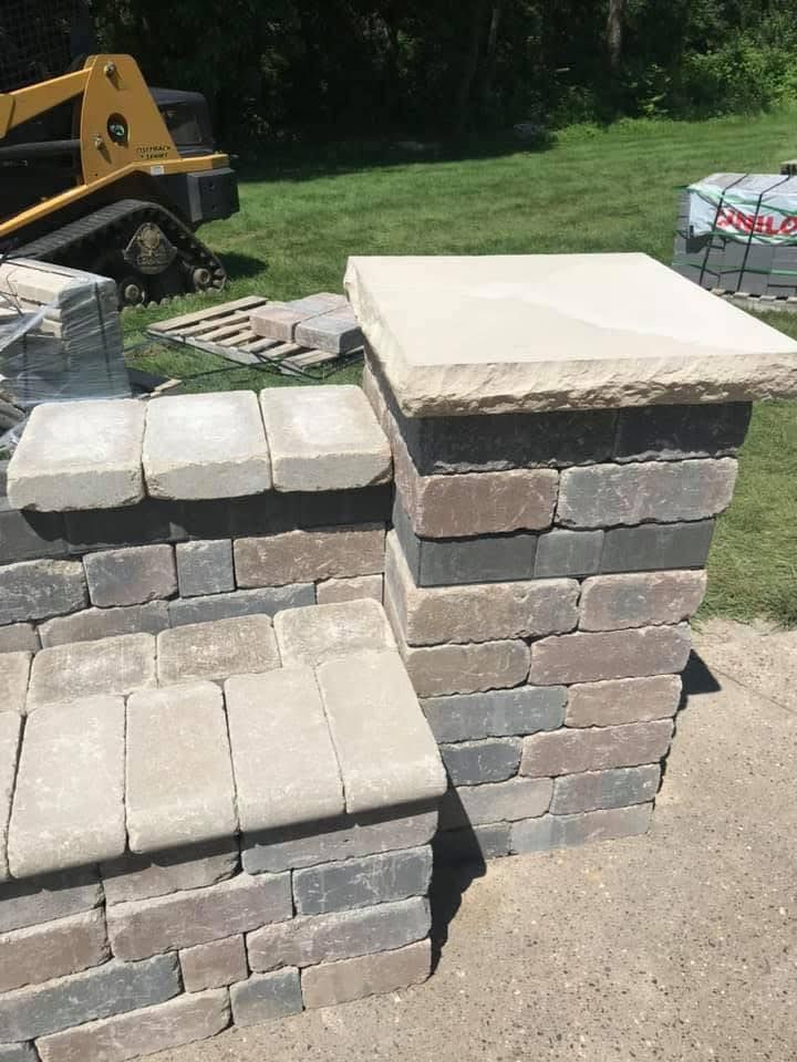 Stacked stone retaining wall blocks beside a driveway with construction equipment in the background