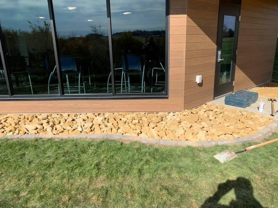 Modern building exterior with large windows, stone landscaping, and a grassy foreground