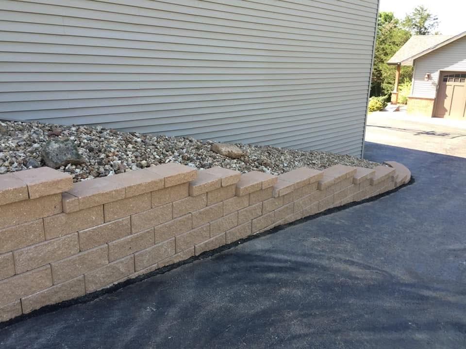 Brick retaining wall beside asphalt driveway along a house exterior