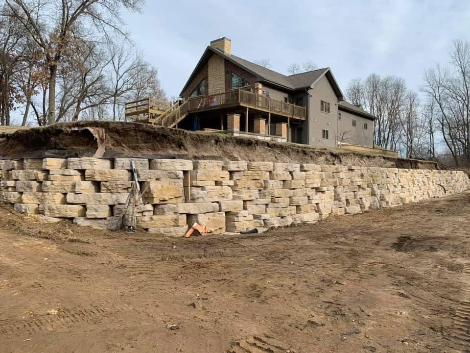 Large stone retaining wall supporting a tan house on a bare hillside in winter