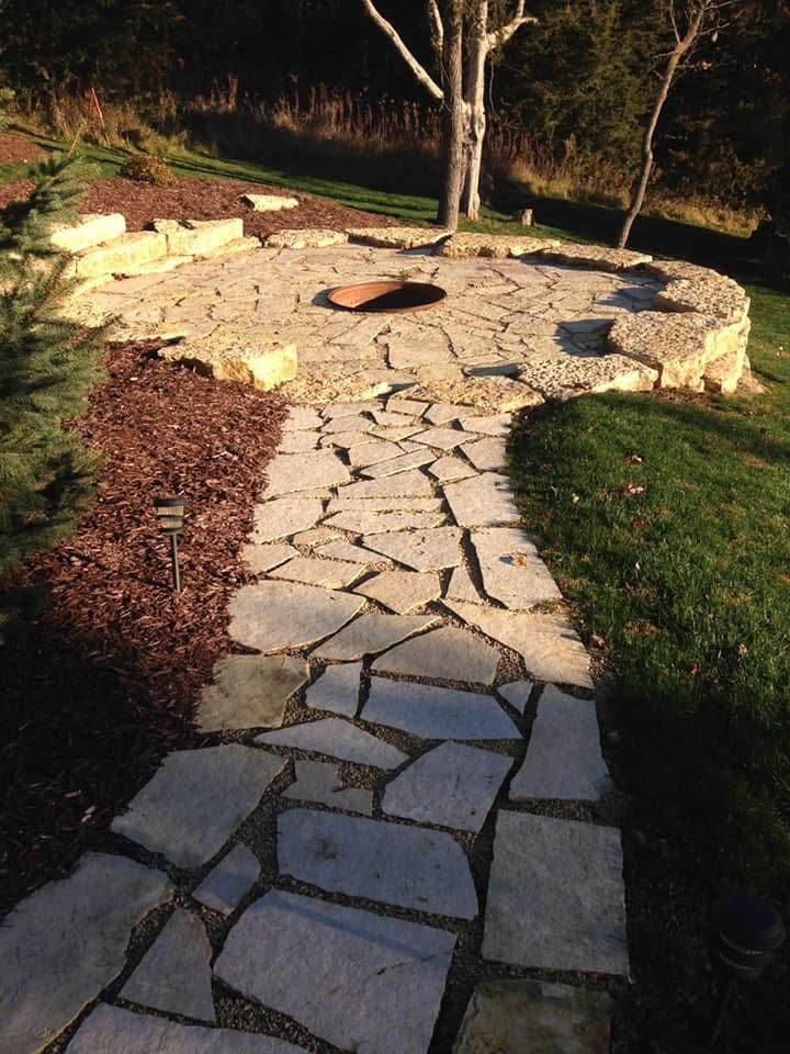 Stone garden path leading to a circular patio with a tree, rocks, and grass around it