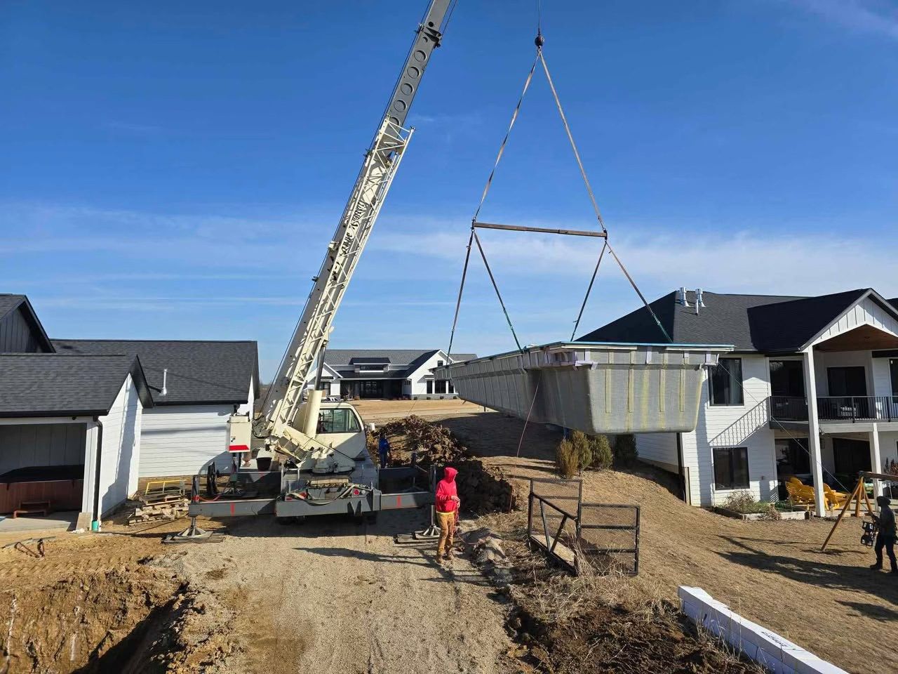 Crane lifting a roof truss on a new housing construction site, with workers below.
