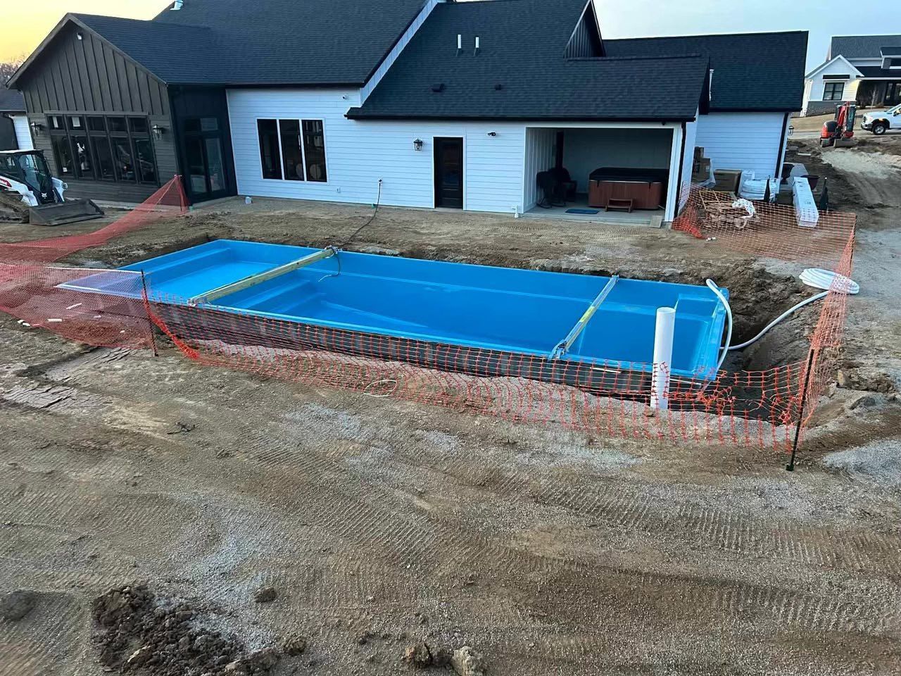 Backyard in construction with a blue covered pool beside a house and brick edging