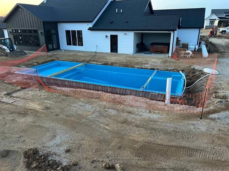 Covered rectangular pool area beside a white house, surrounded by orange safety fencing