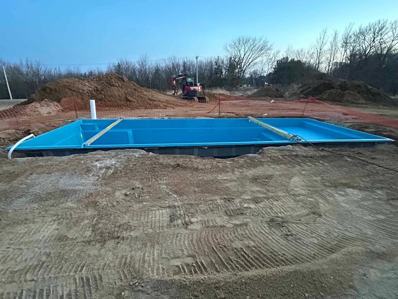 Blue foundation frame on a dirt lot, with a small tractor in the background under a clear sky.