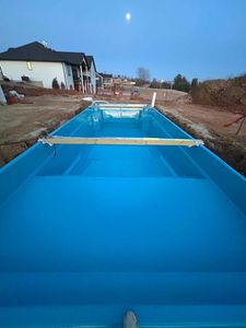 Bright blue backyard pool under construction with a wooden plank across it at dusk