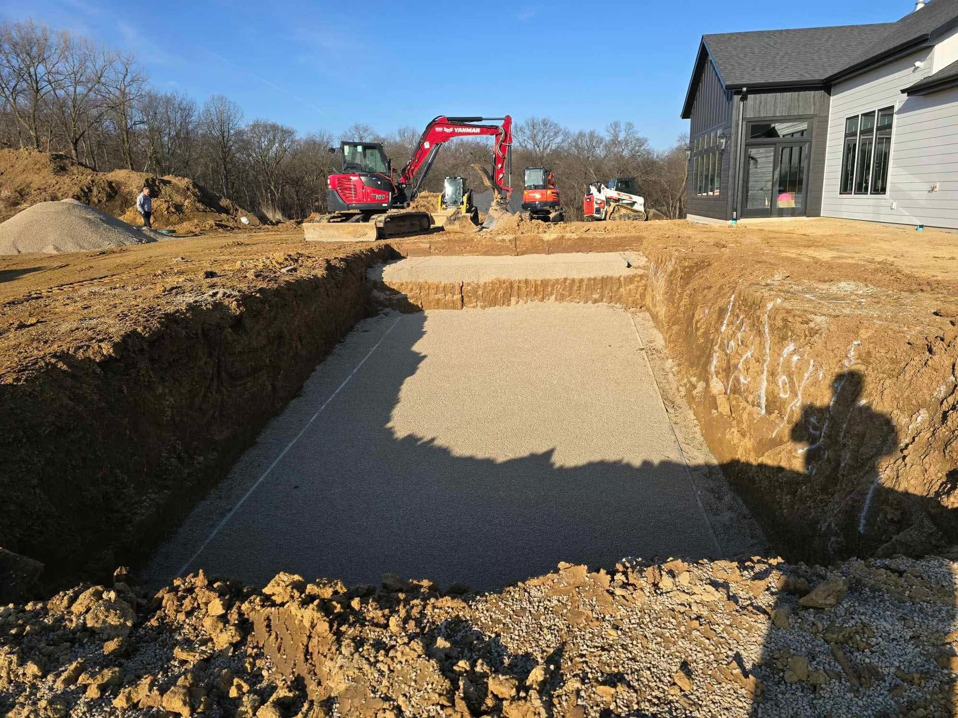 Construction site with a red excavator digging a large trench beside a house.