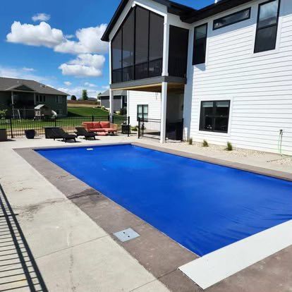 Backyard pool covered with blue tarp beside a white two-story house and patio furniture