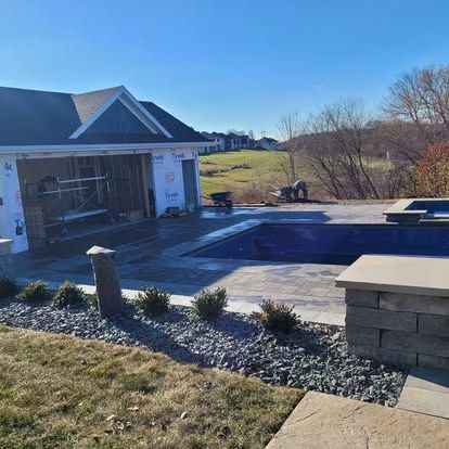 Backyard patio with a house, covered pool, stone landscaping, and winter grass under a clear blue sky