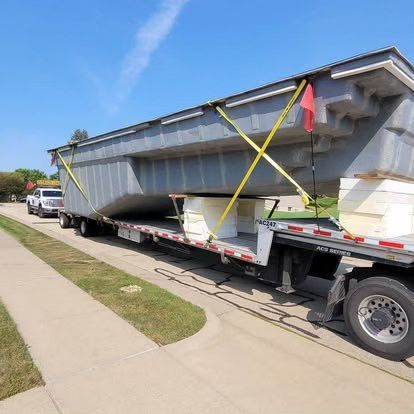 Large metal beam secured with straps on a flatbed trailer parked beside a sidewalk