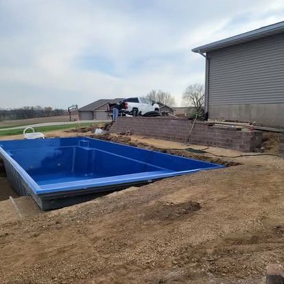 Blue in-ground pool under construction beside a house in a dirt yard