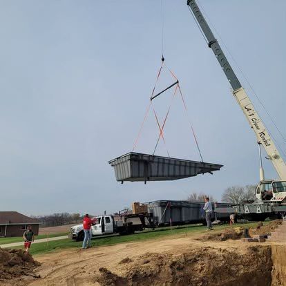 Crane lifting a large dark container over a construction site on a cloudy day.