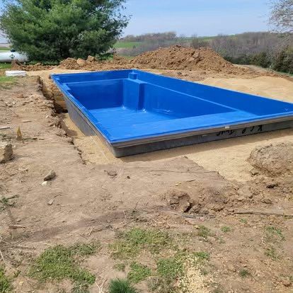 Blue rectangular in-ground pool under construction in a dirt lot with piles of soil around it