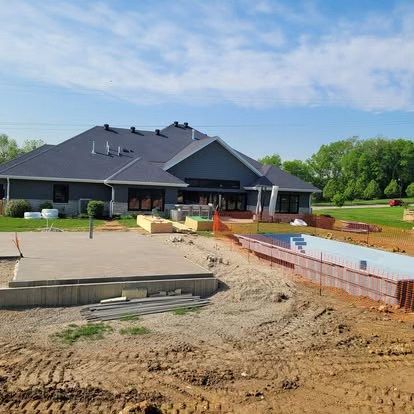 New house under construction with dirt driveway, concrete foundation, and red brick edging