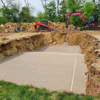 Excavators dig a large pit around a concrete slab at a construction site.