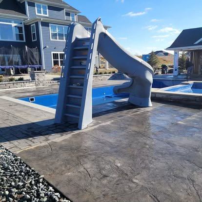 Blue pool slide beside a house, set on a concrete patio under a clear sky.