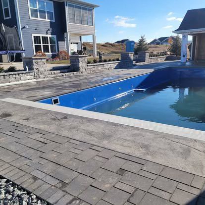Empty backyard swimming pool with blue lining, stone patio, and houses in the background
