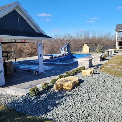 Backyard pool with diving board, covered pavilion, and gravel landscaping on a sunny day