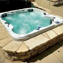 Hot tub with bubbling blue water on a stone patio in bright sunlight