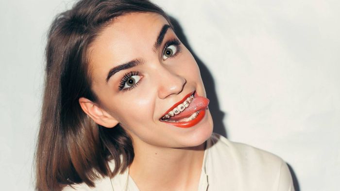 Una mujer con brackets en los dientes saca la lengua.