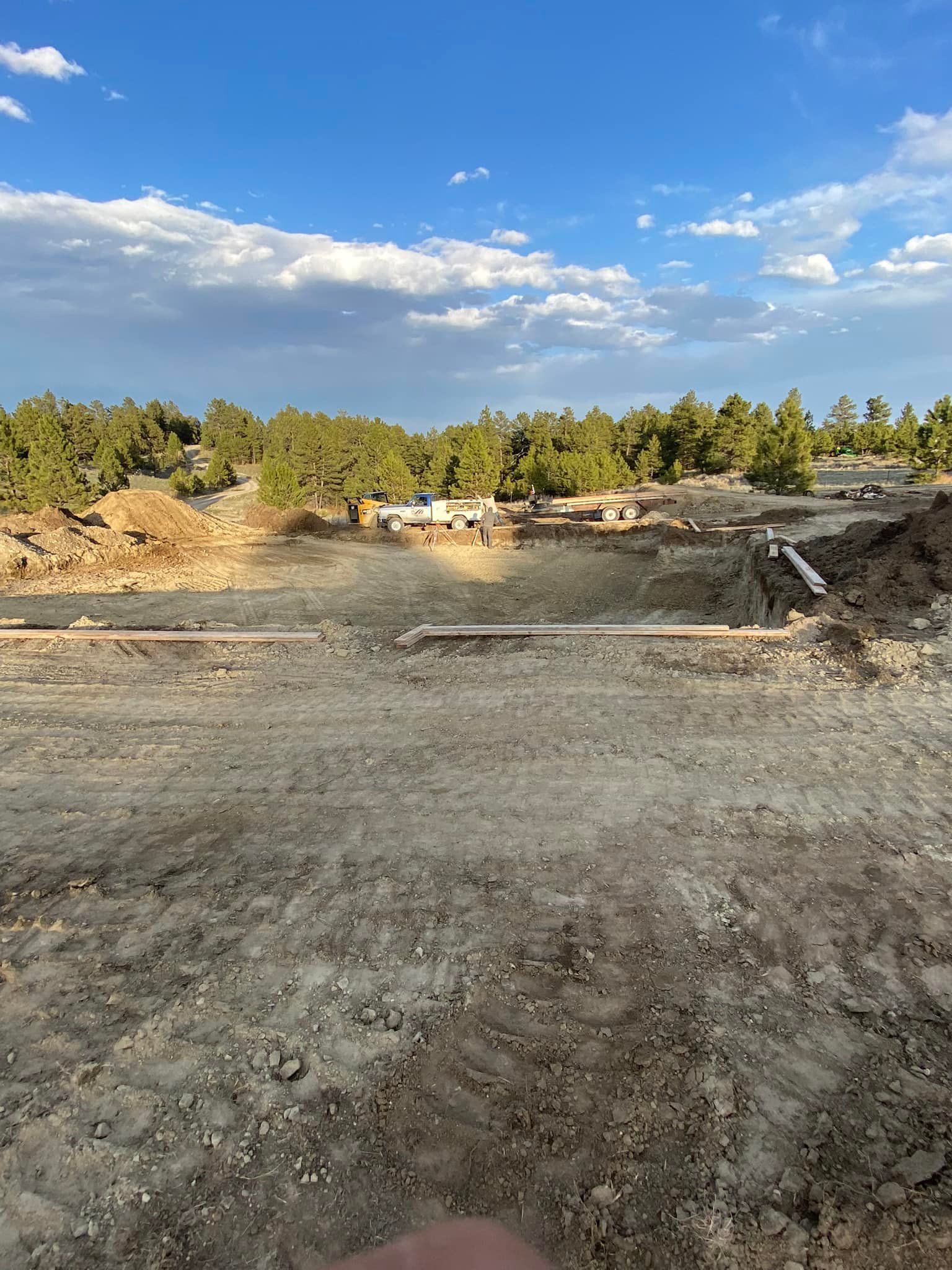 Dirt construction site with trees and blue sky.