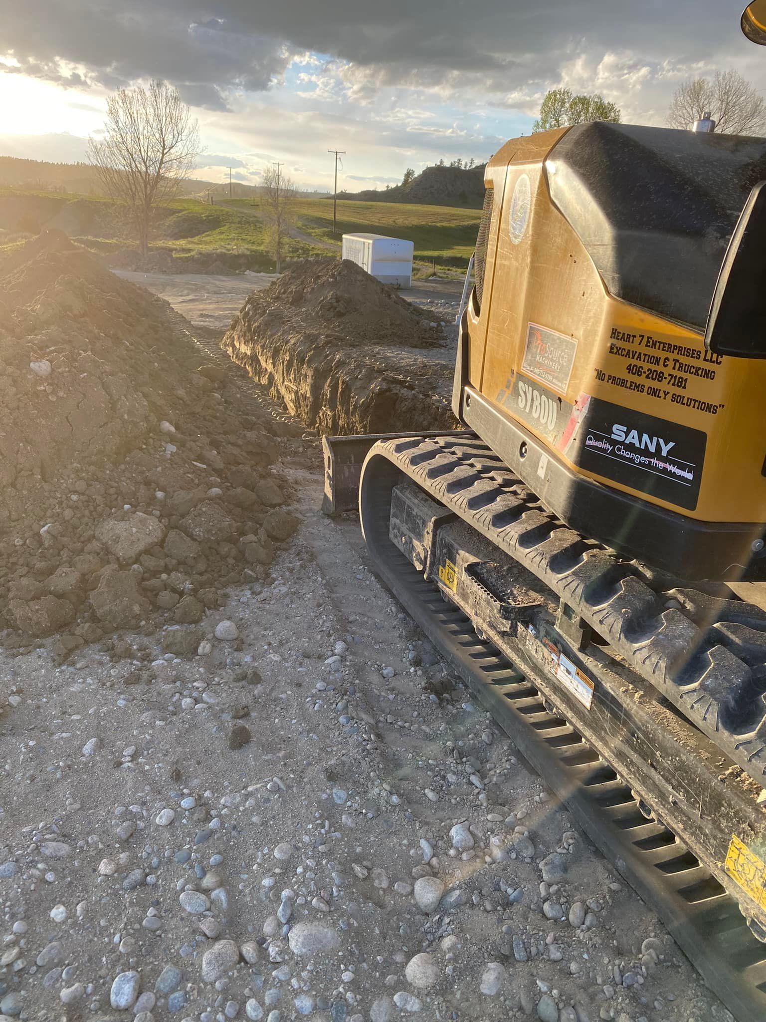Yellow excavator digging a trench in a construction site with dirt pile and overcast sky.