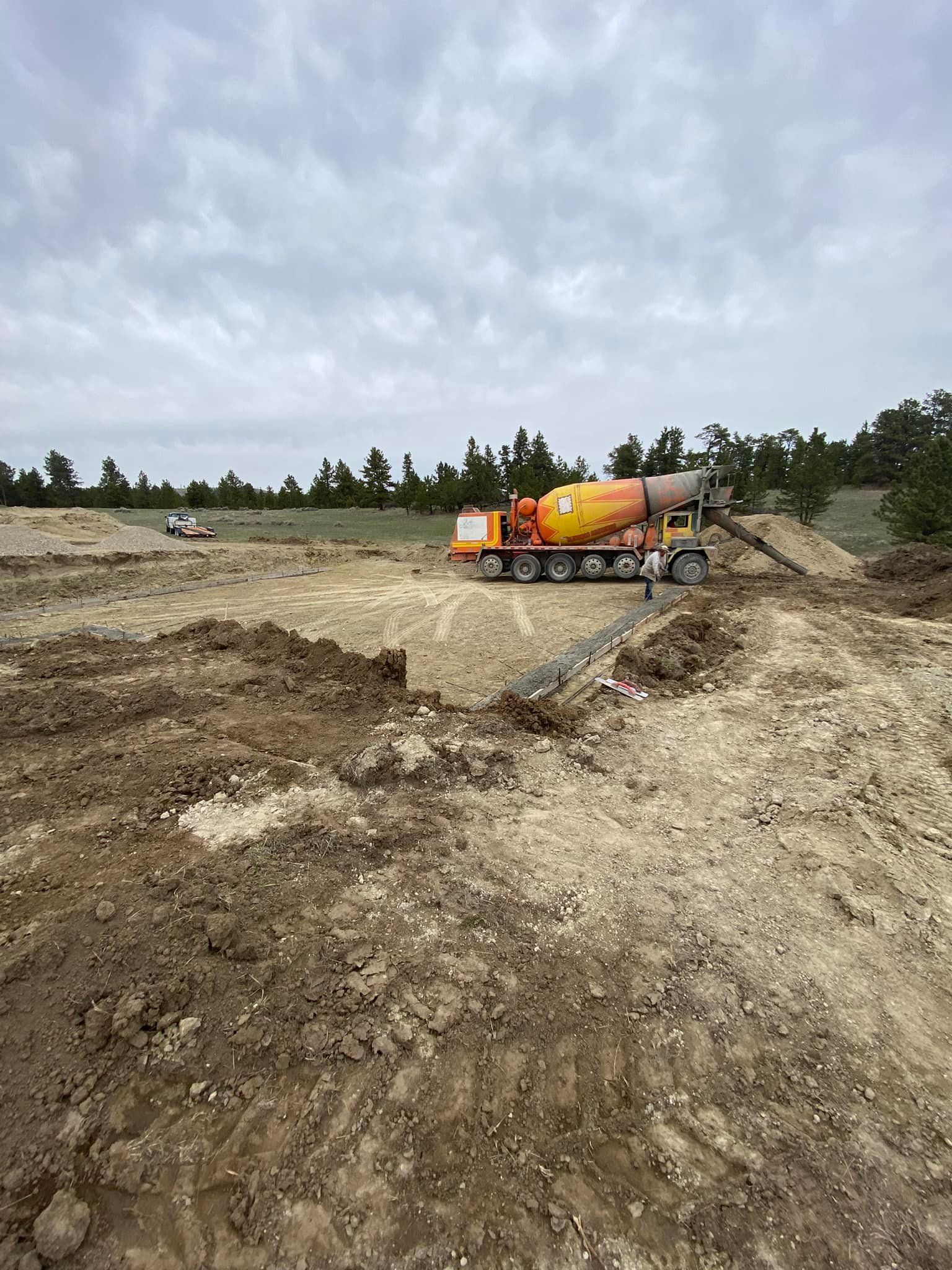 A concrete truck pours cement into a construction site excavation on an overcast day.