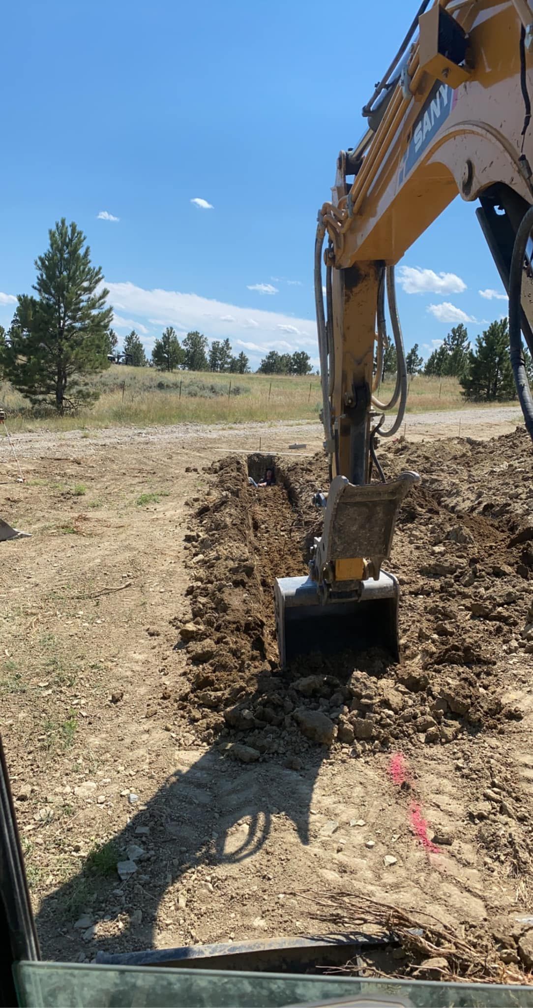 An excavator digging a trench in dirt on a sunny day.