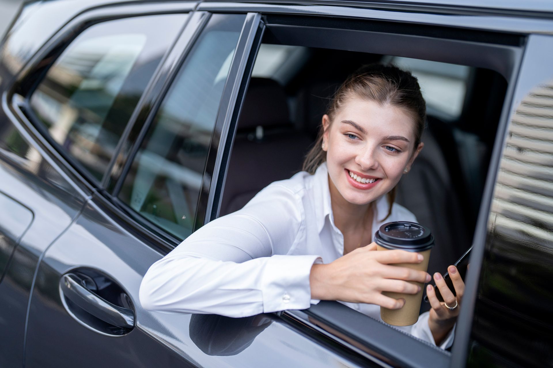 A woman is sitting in a car holding a cup of coffee and looking out the window.