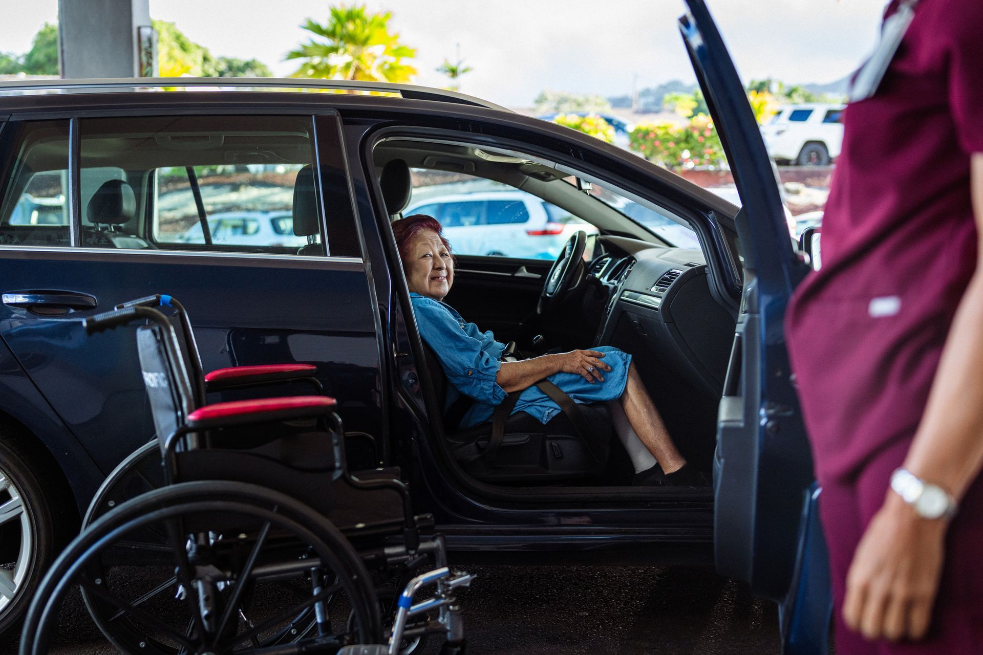 A woman in a wheelchair is sitting in a car next to a nurse.